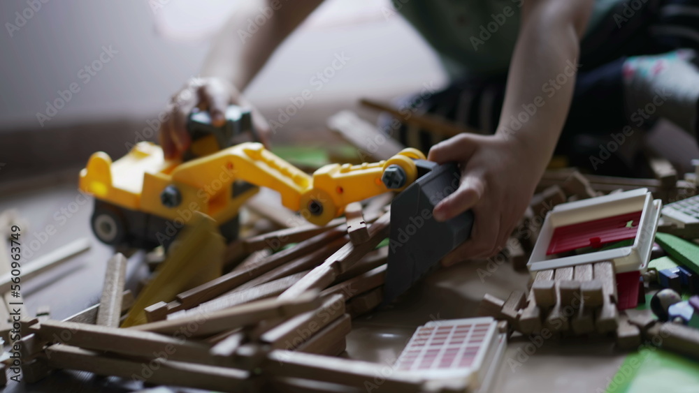Kid plays with bulldozer tractor toy picking pieces of wood playing at home playroom. Closeup child hands