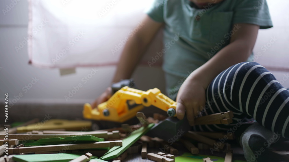 Kid plays with bulldozer tractor toy picking pieces of wood playing at home playroom. Closeup child hands Kid plays with bulldozer tractor toy picking pieces of wood playing at home playroom. Closeup child hands
