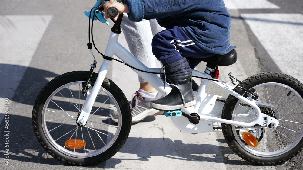 Obraz premium Child cyclist crossing street with mother on zebra lines crosswalk. Little kid riding bicycle outdoors