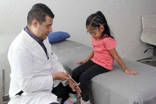 Latino doctor medic and girl patient in medical office checks her reflexes on hammer in her checkup to find disease diagnosis