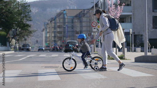 Child crossing street in city crosswalk with mother outdoors photo