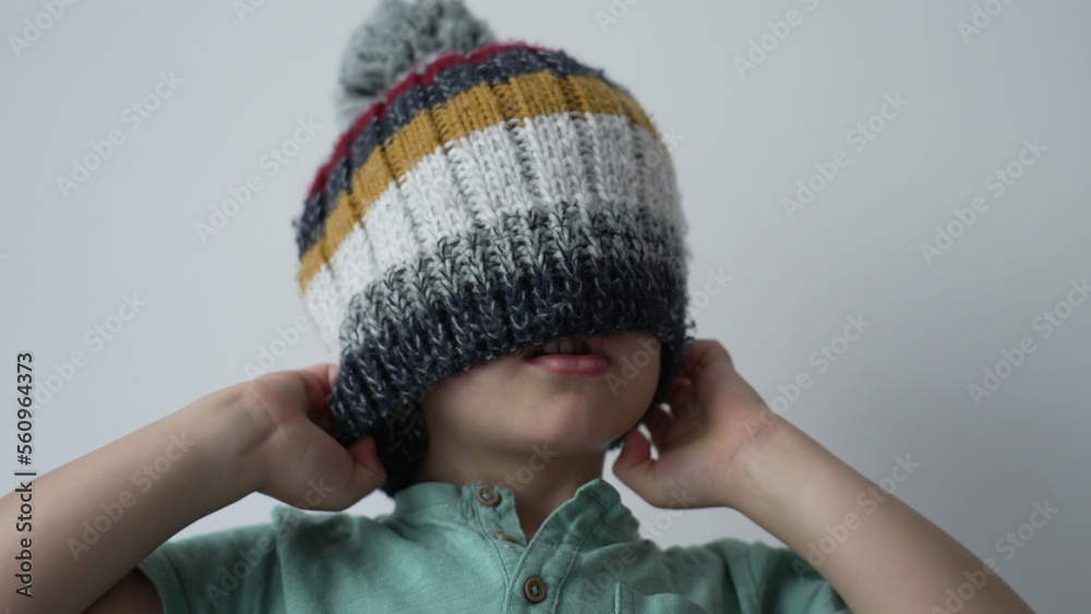 One little boy putting beanie covering face. Funny child wearing wool winter clothing accessory One little boy putting beanie covering face. Funny child wearing wool winter clothing accessory