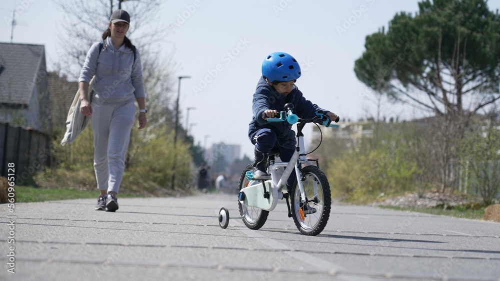 Fototapeta premium Little boy learning to ride bicycle outside in green pathway during winter season. Child learns to bike outdoors