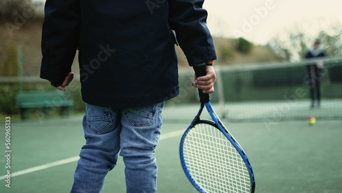 Back of kid playing tennis with parent during winter season. Child wearing coat and beanie hitting ball. Small boy plays sport outdoors © Marco