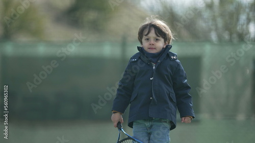 Portrait little boy wearing coat during autumn season holding tennis racket outdoors