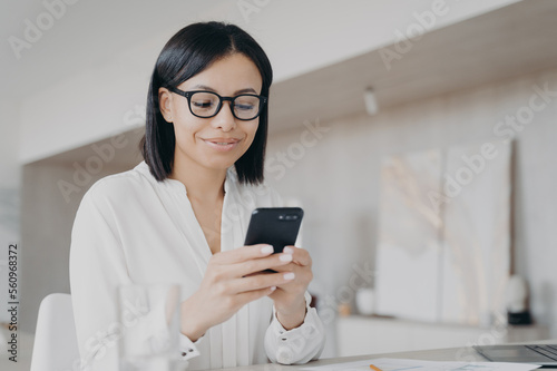 Businesswoman in glasses using phone mobile apps in office, reads good news message, chatting online