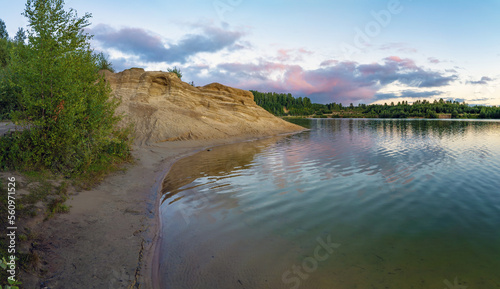 A high cliff on the shore of a lake with colorful clouds in the sky at sunset.