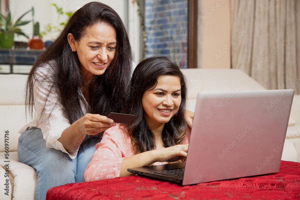 Two Indian women are using credit card doing online shopping on laptop at home. Two Indian women are using credit card doing online shopping on laptop at home.