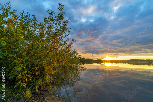 The bright sun illuminates the dark sky at sunset and is reflected in the lake .