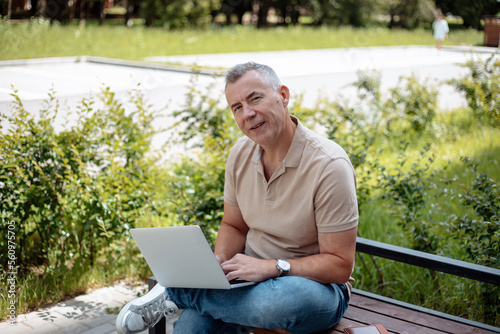 Expressive, charismatic senior gray haired businessman using laptop, wireless modern technology sitting on bench in park