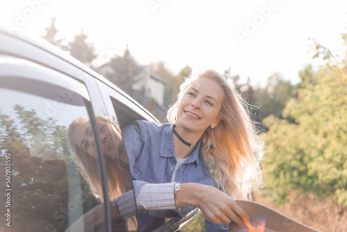 Glad, pensive, smiling, proud blond woman hold hat in hands, leaning out of car window on backseat. Journey, travelling