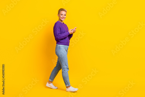 Full size profile photo of positive charming girl use telephone walk empty space isolated on yellow color background