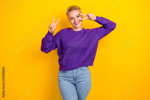 Photo of pretty positive smile youtube blogger blonde hair lady wear trendy violet sweater show v-sign cover face isolated on yellow color background