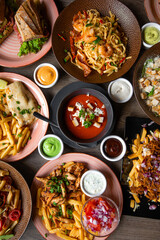 Top view of food on wooden table in restaurant. Pasta with shrimps. Caesar salad with chicken. Sandwiches. Tomato soup.