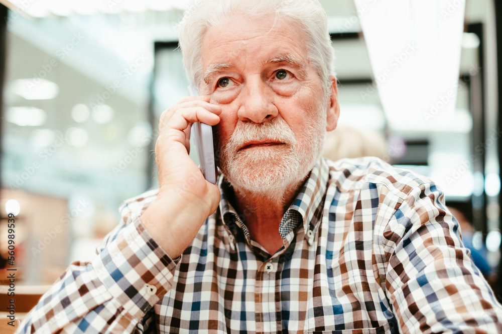 Portrait of a caucasian serious man using mobile phone - handsome bearded elderly man sitting thoughtfully while holding mobile phone Portrait of a caucasian serious man using mobile phone - handsome bearded elderly man sitting thoughtfully while holding mobile phone