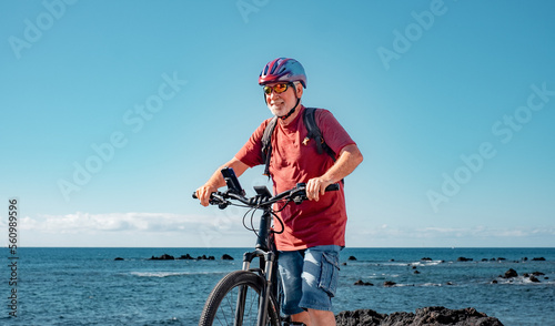 Active senior man enjoying a sunny day at the beach with the electric bicycle. Authentic retirement living and healthy lifestyle concept. Horizon over the sea