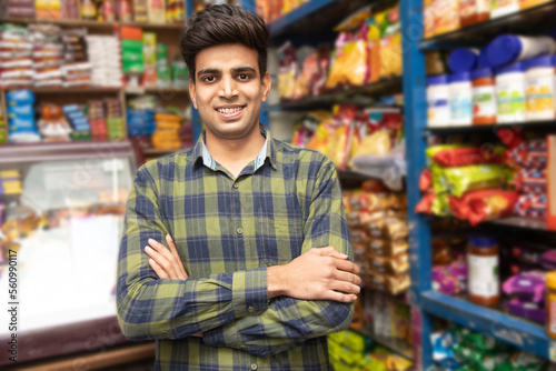 Portrait of smiling handsome young Indian man standing cross arm at grocery shop or supermarket, Closeup. Selective Focus.