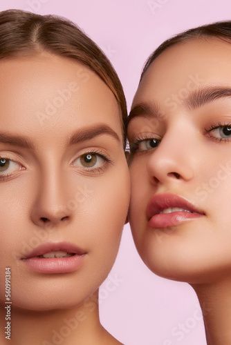 Close-up portrait of two young, beautiful girls with well-kept skin isolated over pink studio background. Concept of skincare, cosmetology, natural beauty