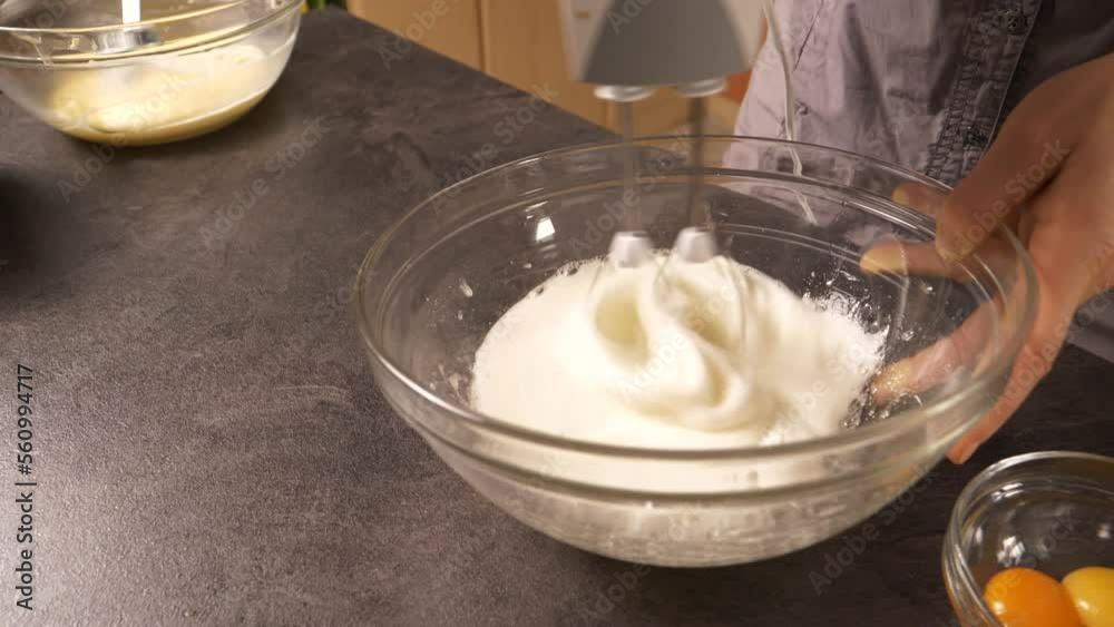 A close-up shot of a young woman using an electric mixer beating the egg white to create foam for a cake filling. A close-up shot of a young woman using an electric mixer beating the egg white to create foam for a cake filling.