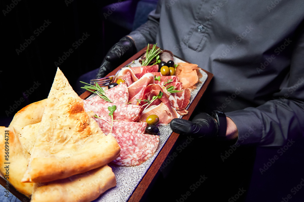 The waiter holds a wooden plate with various sliced dried delicacies