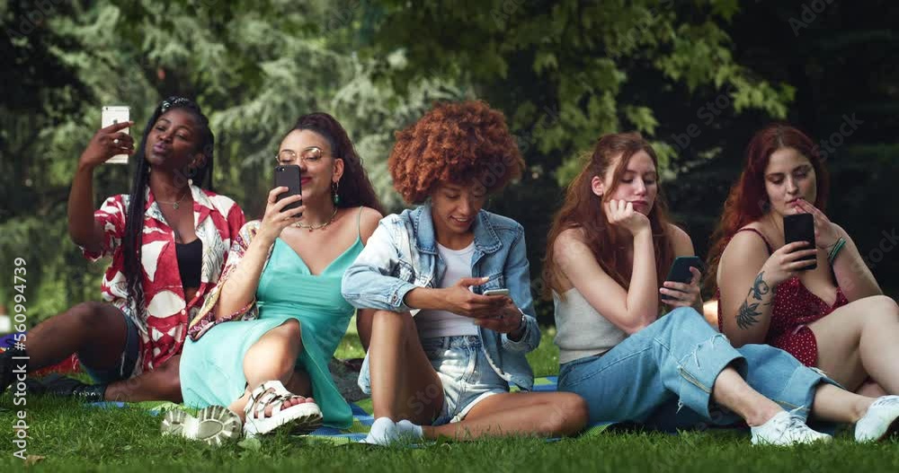 Group of Multiethnic Young Women Using Smartphones While Sitting on Park Lawn. Young Diverse Female Friends Busy with Taking Selfies, Scrolling on Social Media and Posting Instead of Communicating Group of Multiethnic Young Women Using Smartphones While Sitting on Park Lawn. Young Diverse Female Friends Busy with Taking Selfies, Scrolling on Social Media and Posting Instead of Communicating