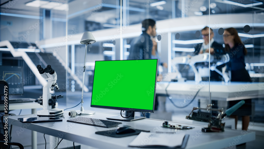 Industrial Research Laboratory with Desktop Computer with Green Screen Mock Up Display. Scientific Lab, Engineering Research Center with Specialists Working on Robot Development in the Background. Industrial Research Laboratory with Desktop Computer with Green Screen Mock Up Display. Scientific Lab, Engineering Research Center with Specialists Working on Robot Development in the Background.