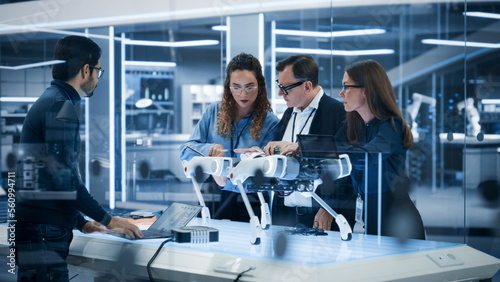 Robotics Engineer, Project Manager and Machinery Operators Collaborate on a Robot Canine Project, Standing with Laptop Computer in Scientific Technology Lab. Young Team Developing an AI Robotic Dog.