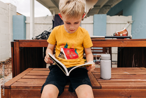 First grader reads a chapter book in backyard on cloudy day photo