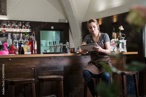 Restaurant owner using tablet while sitting by bar counter