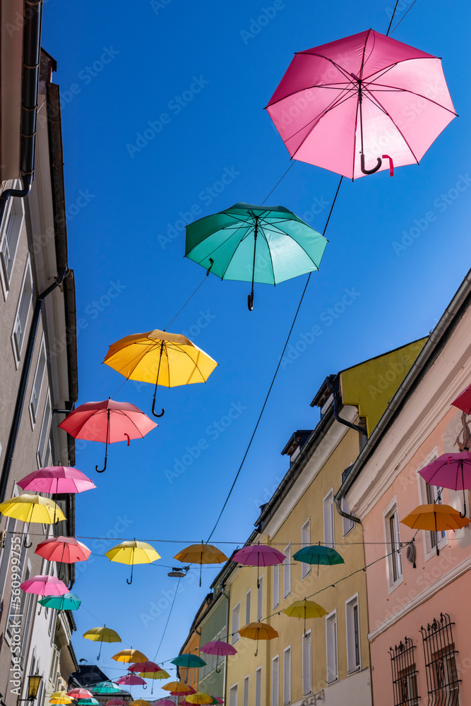 Viele bunte Regenschirme hängen zwischen den Häusern vor einem blauen Himmel