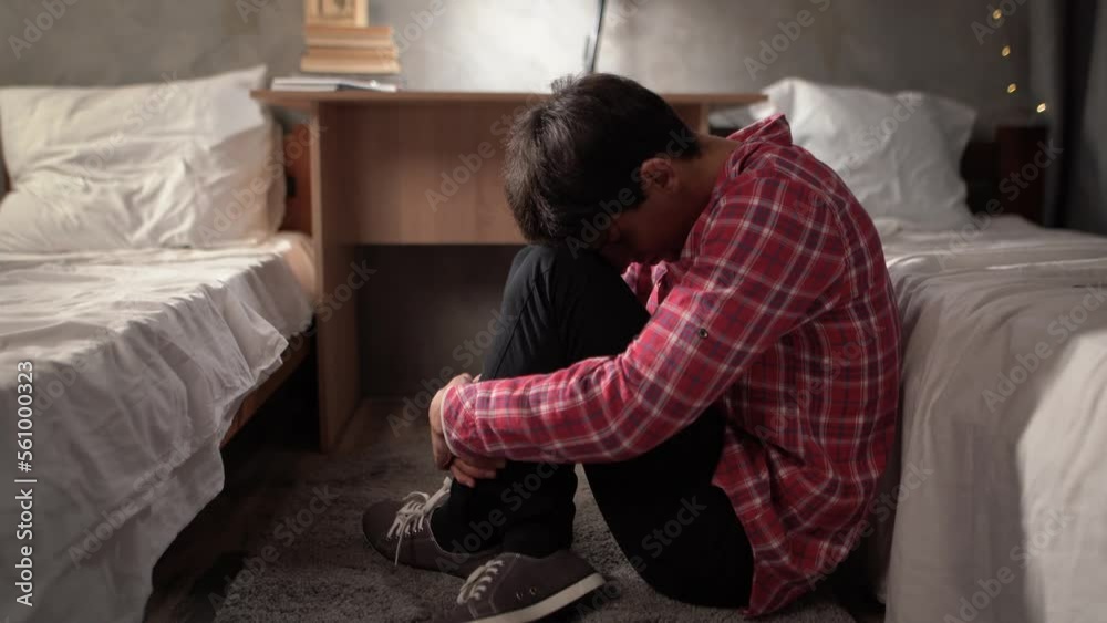 A young arab student sits on the floor in depression in a college dormitory hugging his knees with his hands. Sad man, crying, drama, lonely and unhappy concept. A young arab student sits on the floor in depression in a college dormitory hugging his knees with his hands. Sad man, crying, drama, lonely and unhappy concept.