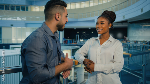 Friendly diverse multiethnic business partners colleagues talking in office hall. African American woman businesswoman and Indian Arabian man businessman talk corporate discussion conversation at work