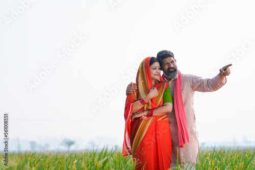 Indian farmer with wife spreading hand and giving expression at field.