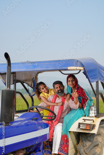 Happy Indian farmer family sitting on tractor at agriculture field.