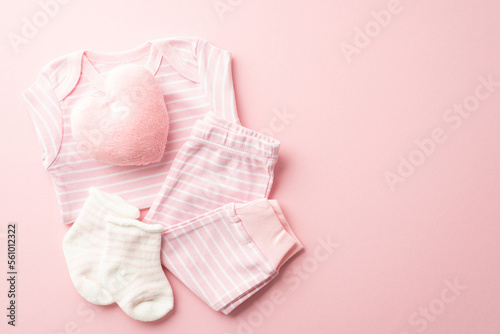 Baby shower concept. Top view photo of pink infant clothes shirt pants socks and heart shaped fluffy toy on isolated pastel pink background with blank space