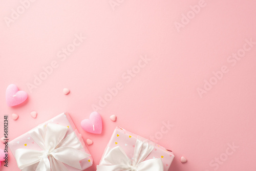 Valentine's Day concept. Top view photo of gift boxes with white ribbon bows heart shaped candles and sprinkles on isolated pastel pink background with copyspace