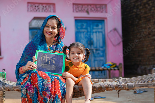 education concept : Indian rural woman showing shiksha words in hindi calligraphy with daughter photo