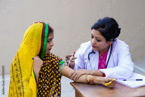 Indian woman doctor injecting to rural woman at clinic photo