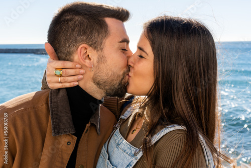 Young boyfriend and girlfriend kissing each other with closed eyes while celebrating Saint Valentine Day against sea