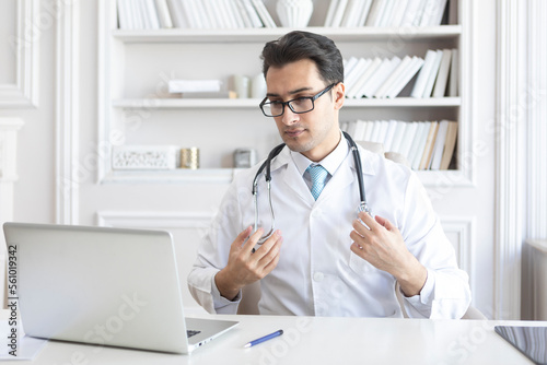Wallpaper Mural Young handsome physician in white medical gown smiling and working with gadgets in his modern workplace	 Torontodigital.ca