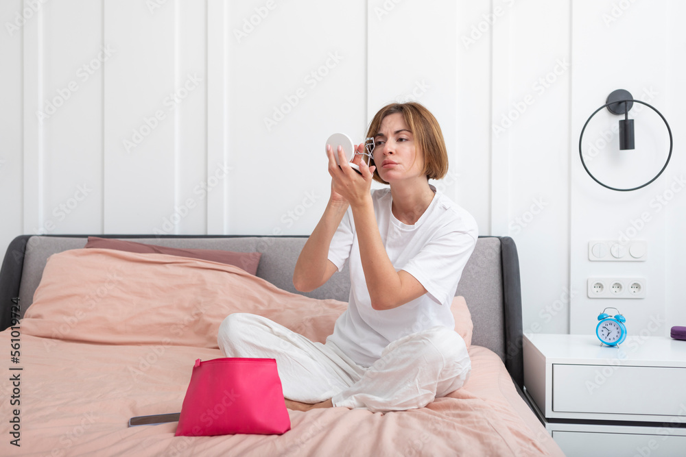 Young attractive woman sitting on the bed and doing make up at the morning time. Female morning routine and preparation concept Young attractive woman sitting on the bed and doing make up at the morning time. Female morning routine and preparation concept
