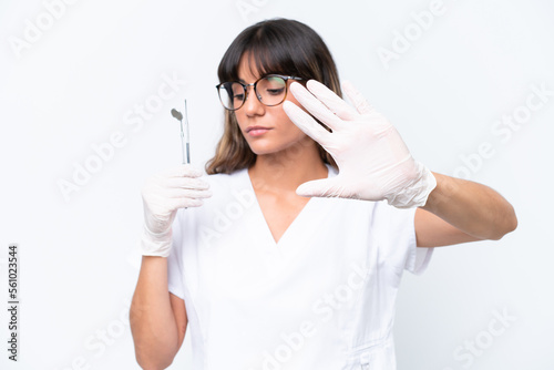 Dentist caucasian woman holding tools isolated on white background making stop gesture and disappointed © luismolinero
