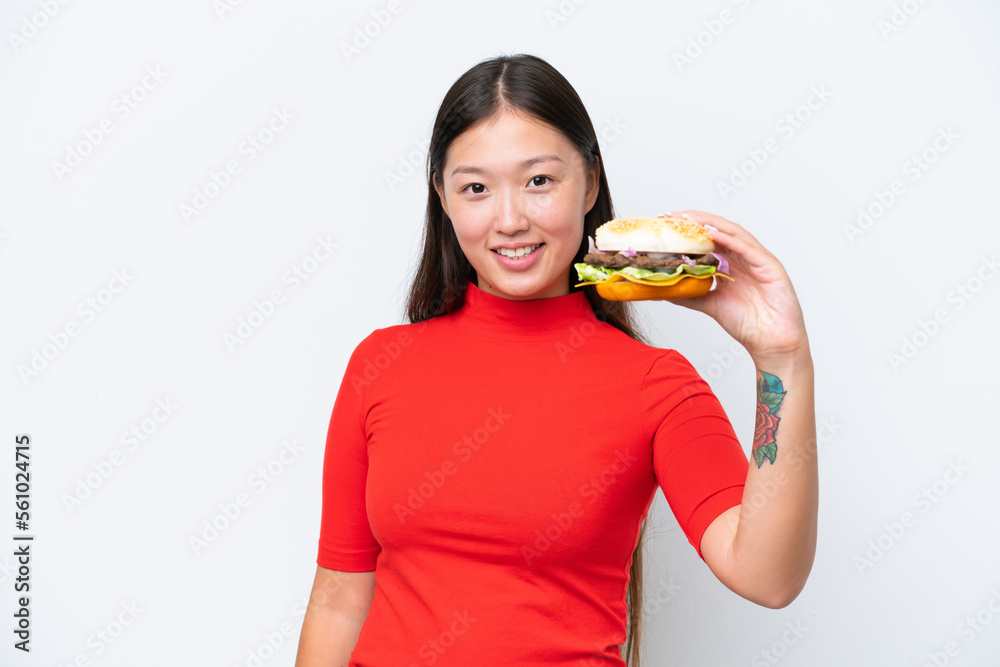 Young Asian woman holding a burger isolated on white background with happy expression Young Asian woman holding a burger isolated on white background with happy expression