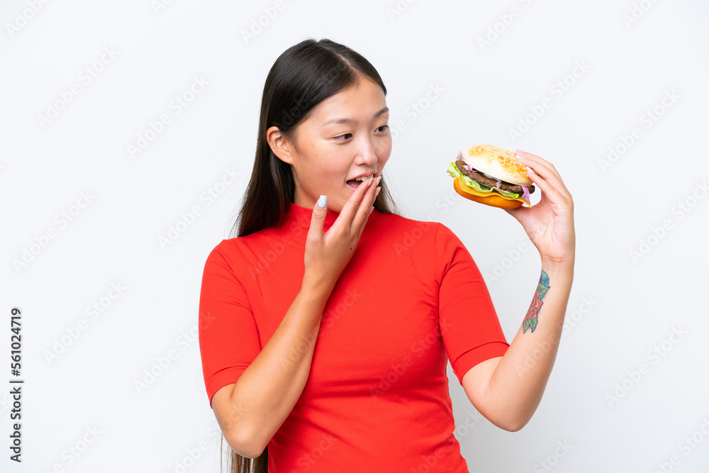 Young Asian woman holding a burger isolated on white background with surprise and shocked facial expression Young Asian woman holding a burger isolated on white background with surprise and shocked facial expression