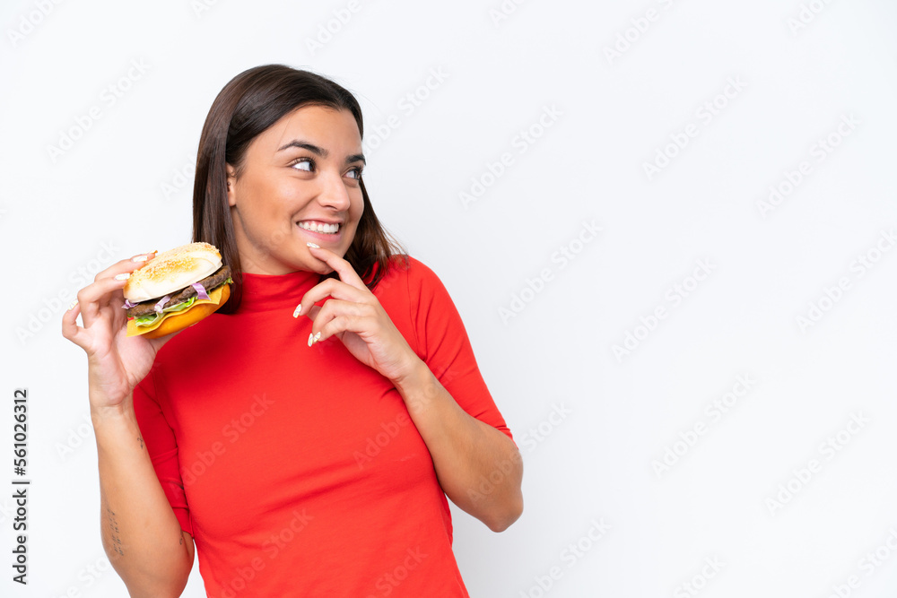 Young caucasian woman holding a burger isolated on white background thinking an idea and looking side Young caucasian woman holding a burger isolated on white background thinking an idea and looking side