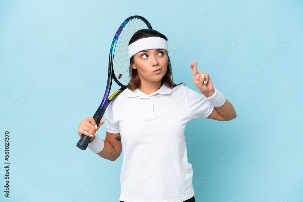 Young tennis player woman isolated on blue background with fingers crossing and wishing the best Young tennis player woman isolated on blue background with fingers crossing and wishing the best