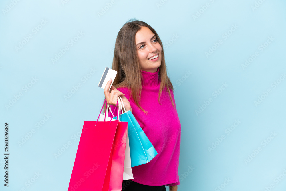 Young beautiful woman isolated on blue background holding shopping bags and a credit card