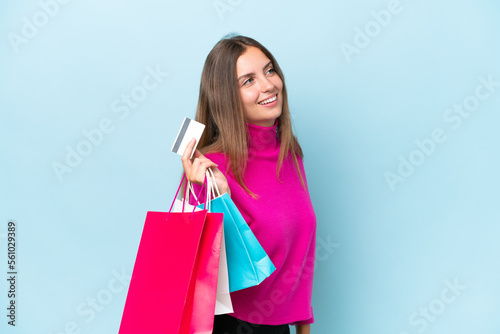 Young beautiful woman isolated on blue background holding shopping bags and a credit card