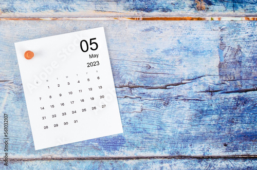 The May 2023 monthly calendar and wooden push pin on blue wooden background.