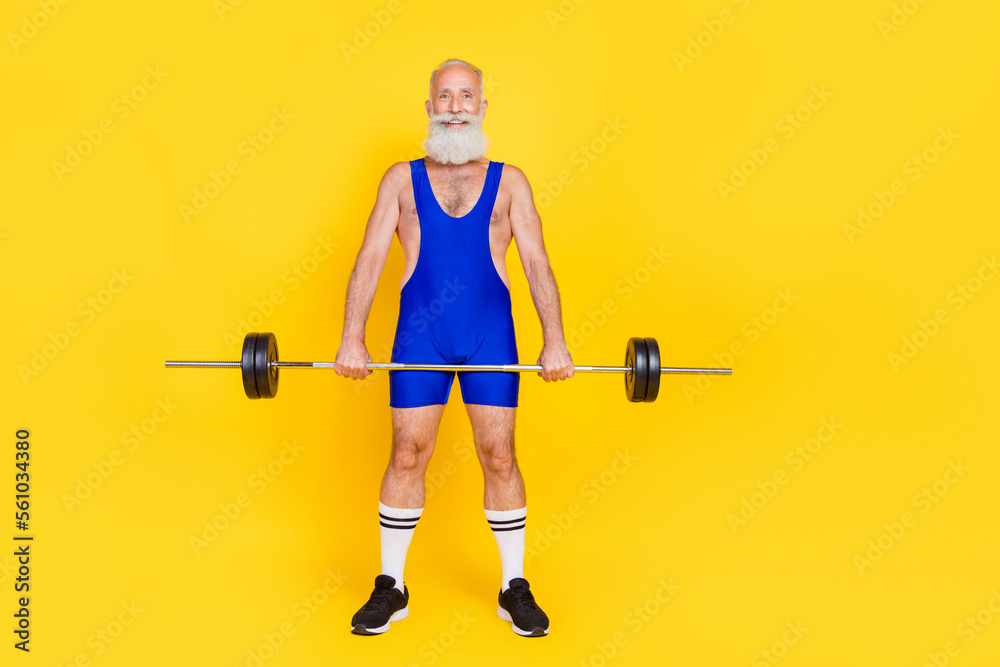 Photo of positive sportive retired guy wear blue overall pumping arms holding barbell empty space isolated yellow color background Photo of positive sportive retired guy wear blue overall pumping arms holding barbell empty space isolated yellow color background